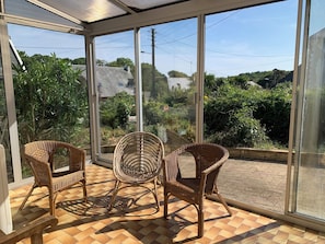 Uma sala de sol com grandes janelas, cadeiras de vime e piso ladrilhado.
