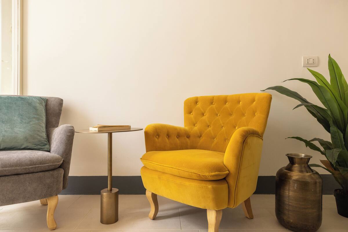 A room with a grey armchair, a yellow armchair, a small round table, and a large potted plant.