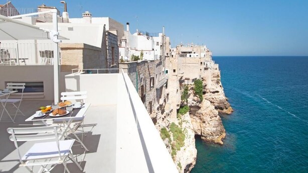 A seaside terrace with dining tables and chairs, overlooking a rocky coastline and the sea. - Dimora Talenti (Polignano a Mare)