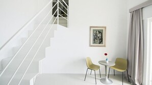A modern room with a white staircase, a framed artwork on the wall, two chairs, and a small table with a vase of flowers. - Dimora Talenti (Polignano a Mare)