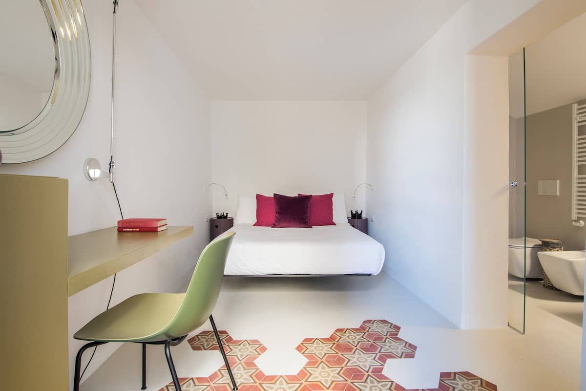 A modern bedroom with a bed, a chair, a bedside table, and a mirror.