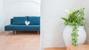 A room with a blue sofa, a white vase with green plants, and a white textured wall. - Dimora Talenti (Polignano a Mare)