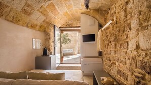 A room with stone walls, a bed, a desk, and a TV. - Dimora Talenti (Polignano a Mare)