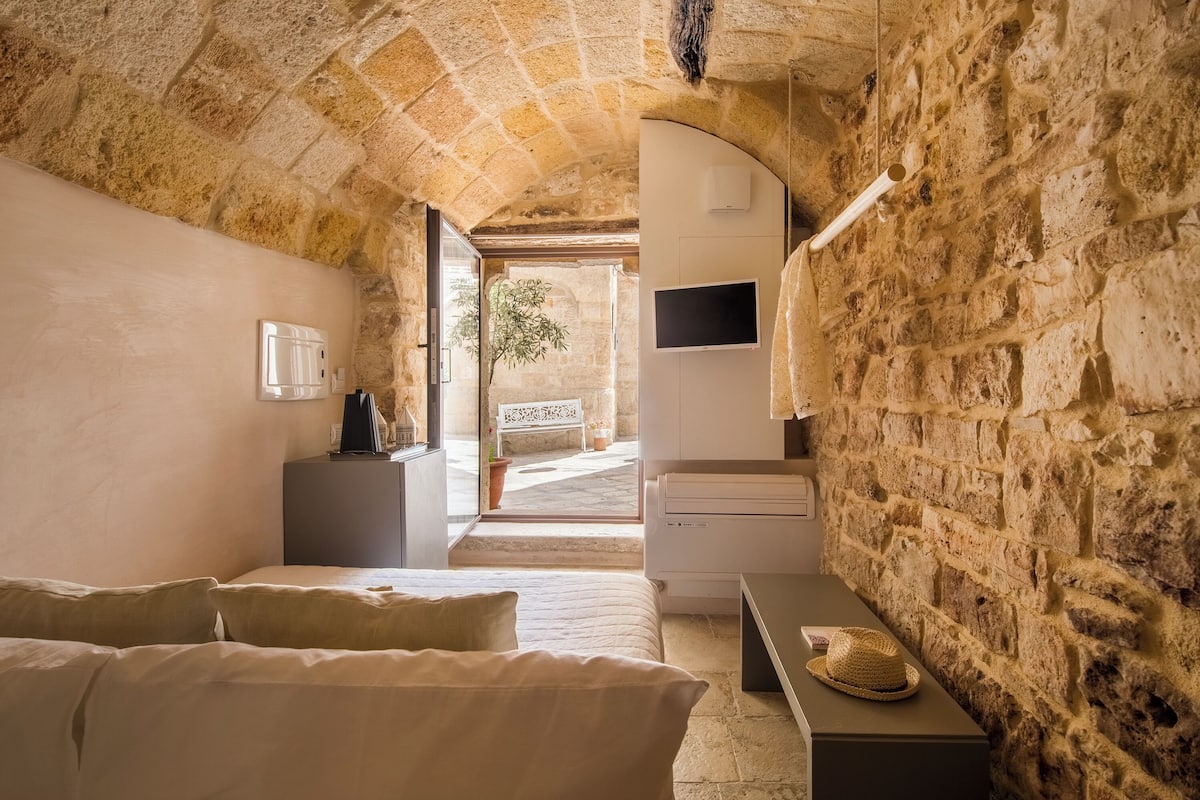 A room with stone walls, a bed, a desk, and a TV.