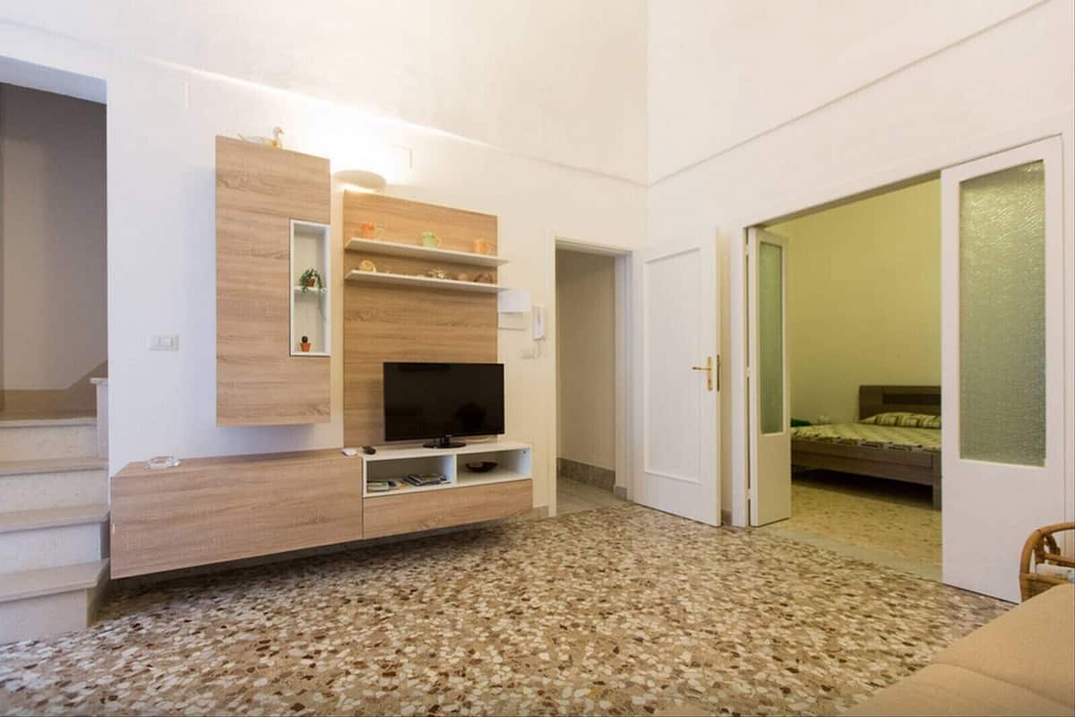A modern room with a built-in TV, a small shelf with decorative items, a door leading to a bedroom, and a carpeted floor.