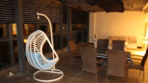 Un comedor con una silla colgante, sillas de mimbre y una mesa.