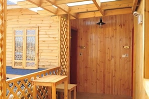 Una baita di legno con un balcone, una porta con un numero e un piccolo tavolo.