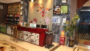 Una zona de recepción con pared de mármol, mostrador rojo, pantalla digital y un cuadro de gran tamaño.