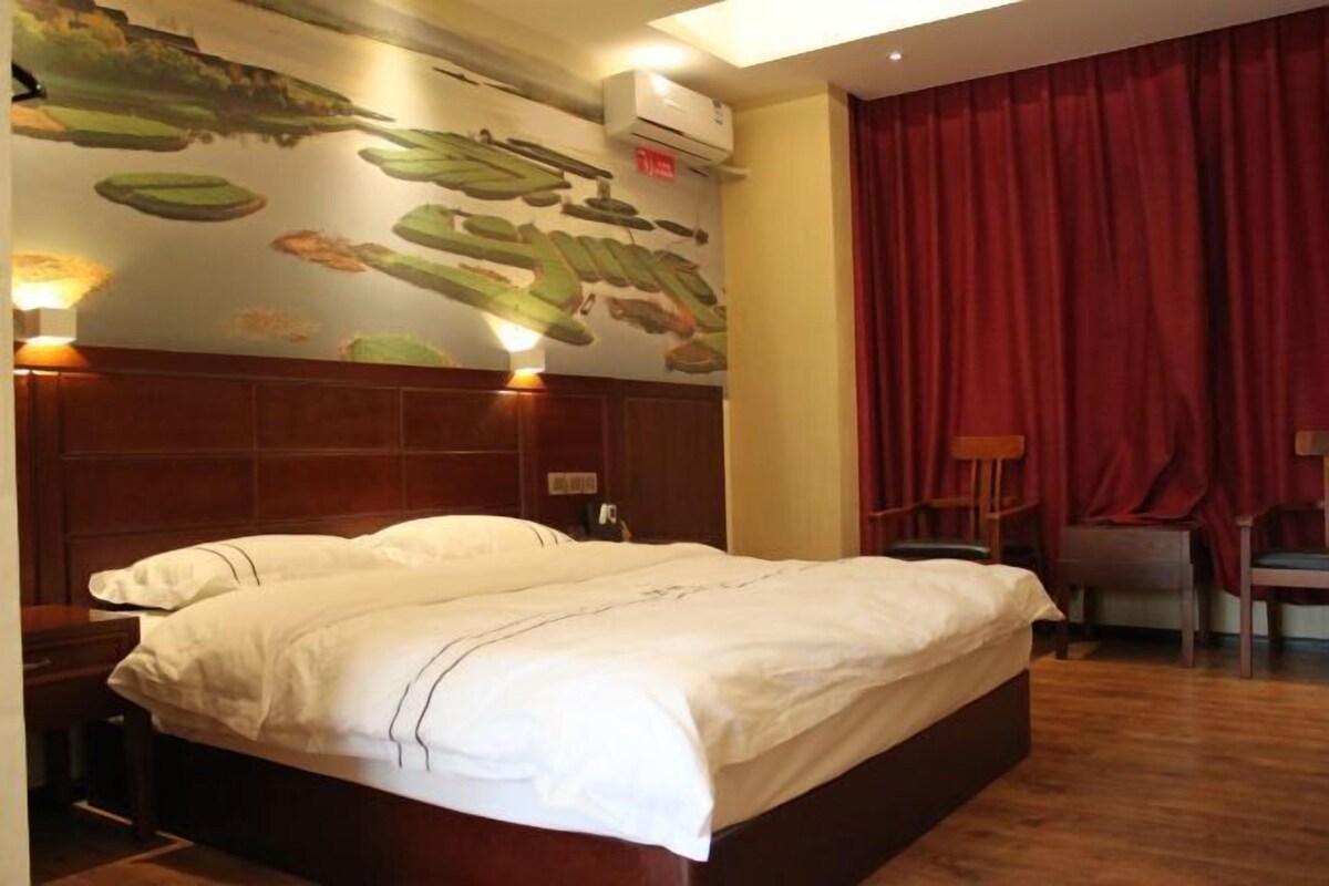 A hotel room with a large bed, a headboard with a mural, a red curtain, and a wooden floor.