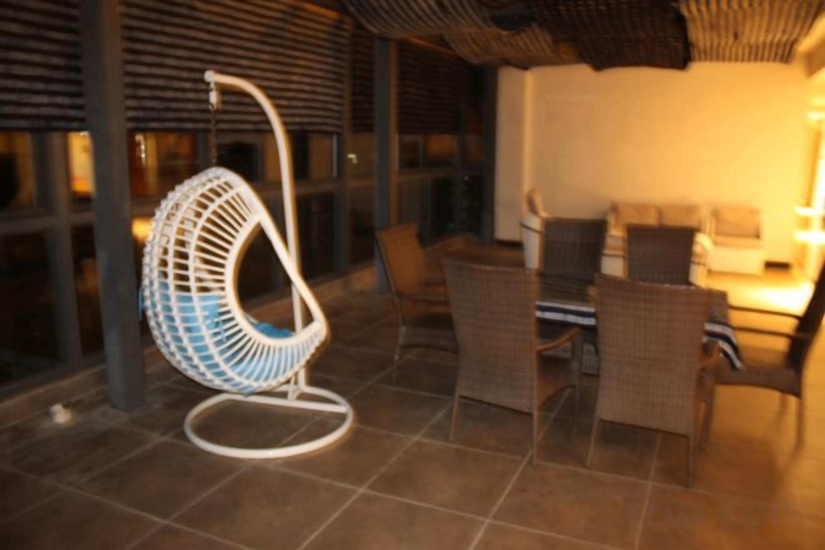 Uma cadeira suspensa, uma mesa de jantar e cadeiras de vime em um espaço interno bem iluminado.