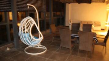 Uma cadeira suspensa, uma mesa de jantar e cadeiras de vime em um espaço interno bem iluminado.