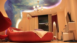 Una habitación con techo curvo, un sillón de mimbre rojo, un televisor de pantalla plana y una araña.