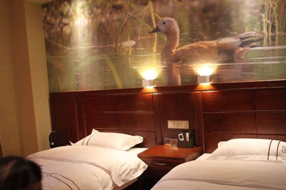 A hotel room with two beds, a wooden headboard, a nightstand with a lamp, and a wall-mounted artwork of ducks in water.