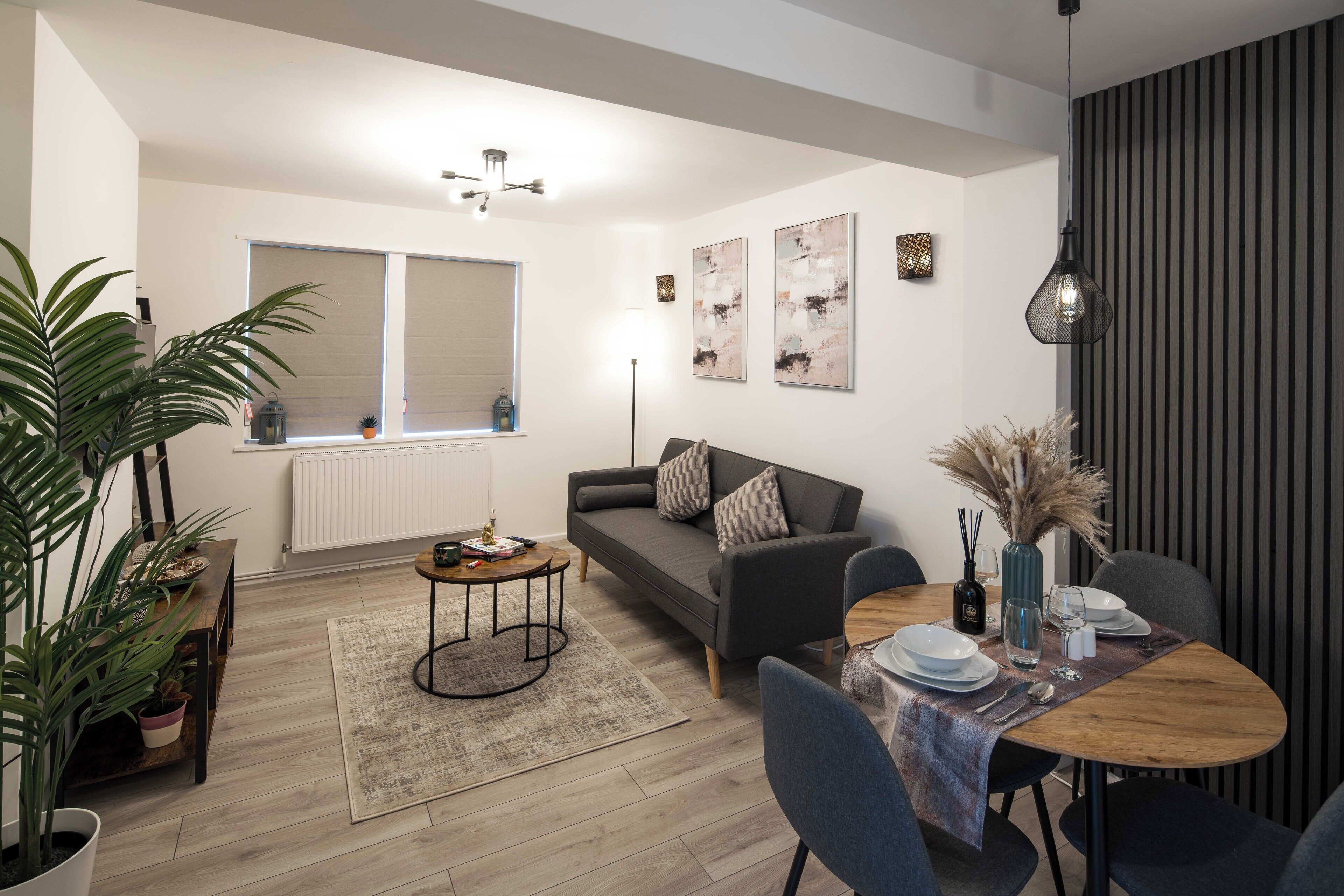 Un salon moderne avec un canapé, une table à manger et des chaises. On y trouve une grande fenêtre, un radiateur et des œuvres d’art murales.