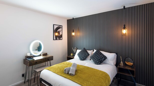 Un dormitorio moderno con cama, mesitas de noche, escritorio con espejo y lámpara de pared.