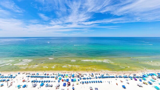 A beach with rows of sunbeds and umbrellas, a clear sky, and calm ocean waters. - Majestic Beach Towers 1-2013 (Panama City Beach)