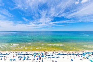 A beach with rows of sunbeds and umbrellas, a clear sky, and calm ocean waters. - Majestic Beach Towers 1-2013 (Panama City Beach)