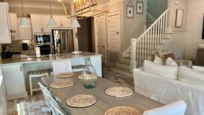 A modern kitchen with white cabinets, a central island, and a dining area with a wooden table and woven placemats. - Town of Prominence- Just Beachy (Santa Rosa Beach)