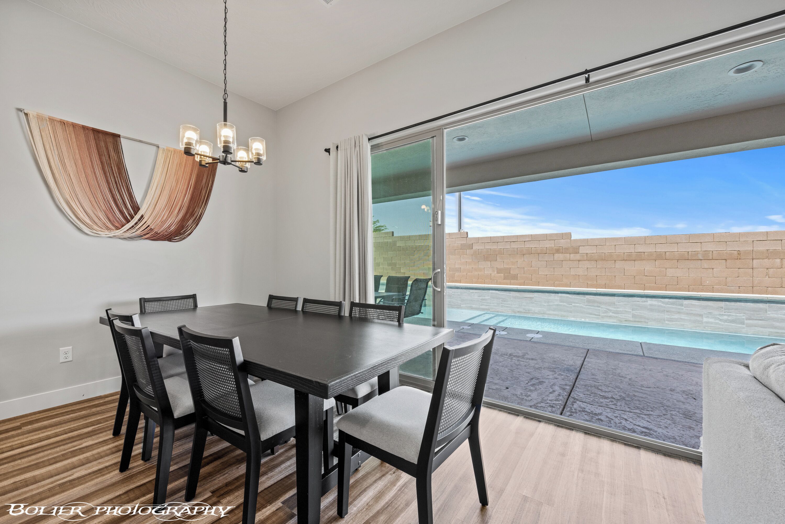 Un espace repas comprenant une table et des chaises, un luminaire suspendu et une vue sur une piscine, visible à travers des portes vitrées.