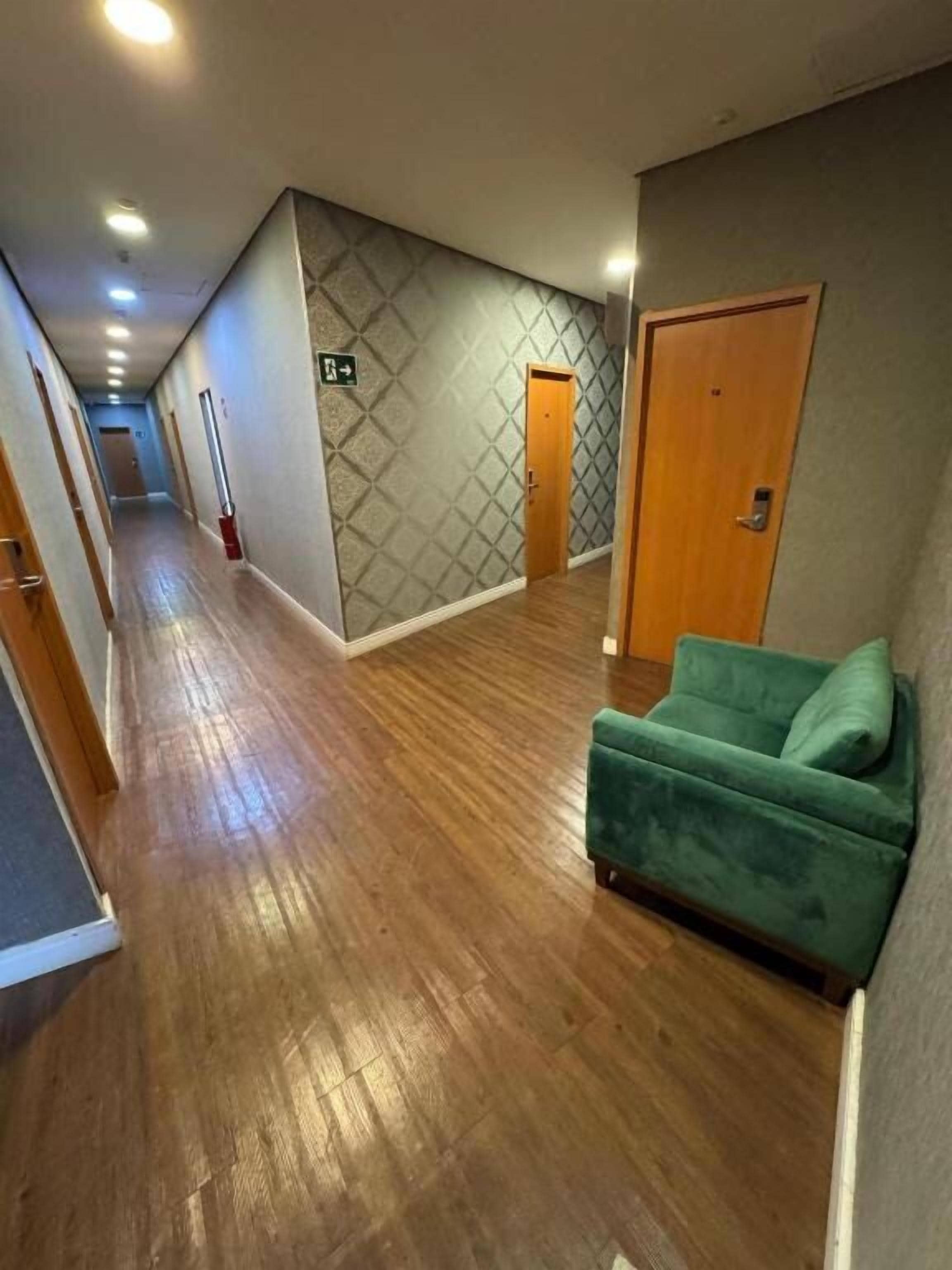 Un couloir doté d’un plancher en bois, d’un canapé vert et d’un mur orné de motifs.