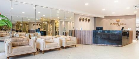 A hotel lobby with sofas, a reception desk, and a large mirror reflecting the interior.