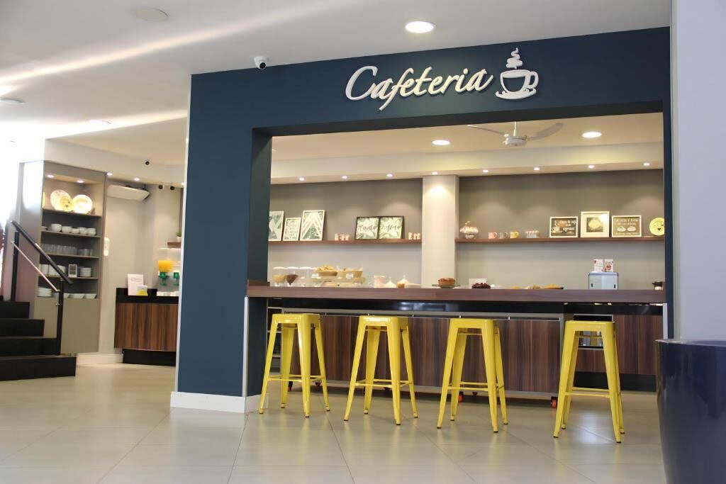 Ein modernes Café mit blauem Eingang, einer Theke mit gelben Hocker und gerahmten Bildern an der Wand.
