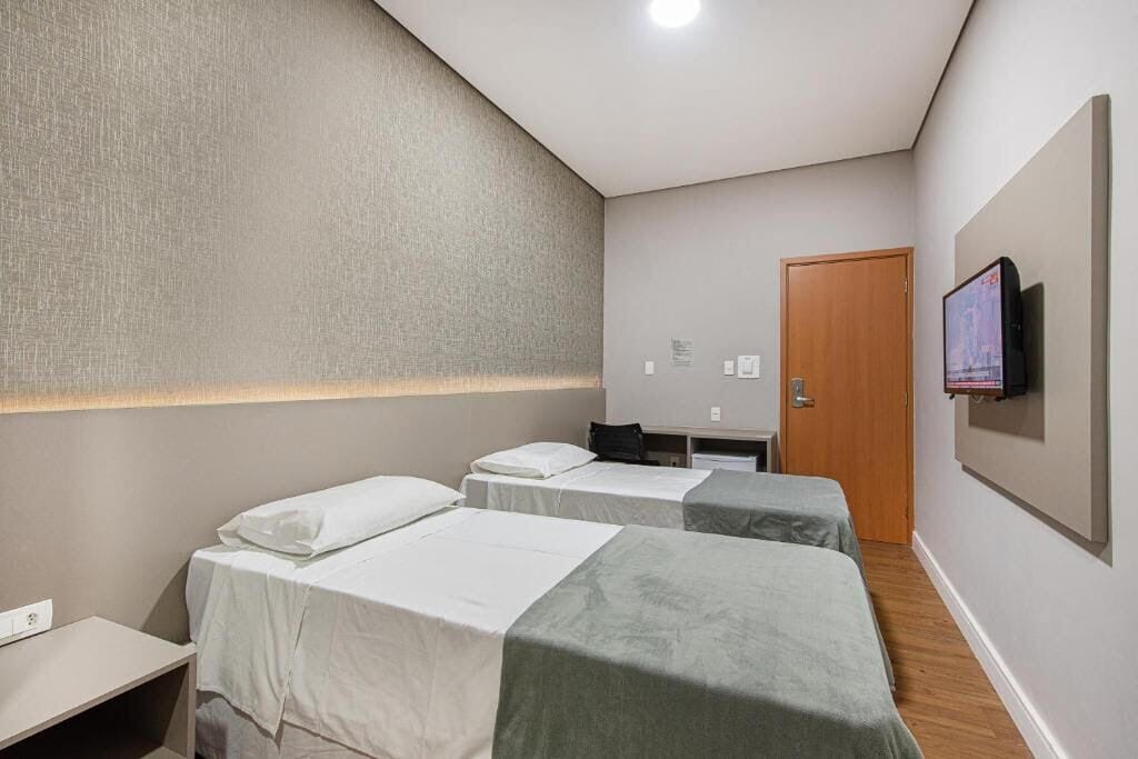 A hotel room with two single beds, a desk, a chair, a television mounted on the wall, and a door.