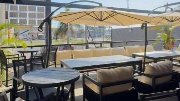 Un espace extérieur aménagé avec des tables et des chaises, une partie couverte avec des parasols, et une vue sur le paysage urbain.