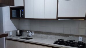 A kitchen with white cabinets, a microwave, a gas stove, and an oven. - Apartamento Completo Mobiliado com ar Condicionado Quente Frio (Country Cascavel)