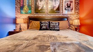 A bedroom with a brick wall, a bed with a wooden headboard, and posters on the wall.