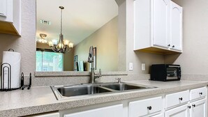 A kitchen with white cabinets, a double sink, a toaster, and a stainless steel range hood.