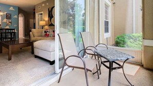 A room with a sofa, a dining table, and chairs. There is a ceiling fan and a window with a view of greenery outside.