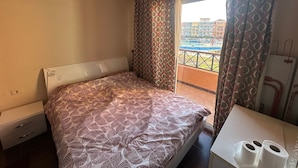 Ein Hotelzimmer mit einem Bett, einem kleinen Tisch mit zwei Toilettenpapierrollen, einem Fenster mit gemusterten Vorhängen und Blick auf einen Gebäudekomplex.