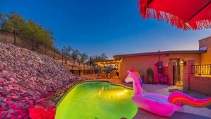 A swimming pool with a unicorn float, surrounded by a stone wall and a wooden deck. - Hilltop Private Resort Home with SPARKLING POOL (Tucson)