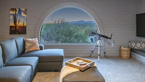 A living room with a large arched window, a telescope, a sofa, and a painting. - Hilltop Private Resort Home with SPARKLING POOL (Tucson)