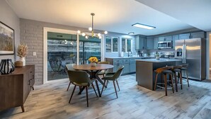 A modern kitchen with a dining area, featuring a large island, stainless steel appliances, and a view to the outside.