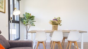 Ein moderner Essbereich mit Holztisch, weißen Stühlen, einer Topfpflanze und einer Lampe.