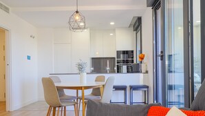 A modern kitchen with white cabinets, a dining area with a white table and chairs, and a sofa with a red and white cushion. - Cubo's Urban Sky Terrace View Apartment / urban / air conditioning / free wifi / community pool (Málaga)
