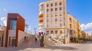 A multi-story building with a curved facade, a staircase leading to the entrance, and a pedestrian crossing in the foreground. - Cubo's Urban Sky Terrace View Apartment / urban / air conditioning / free wifi / community pool (Málaga)
