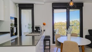 A modern kitchen with a central island, a dining area with a round table and chairs, and a balcony with a view. - Cubo's Urban Sky Terrace View Apartment / urban / air conditioning / free wifi / community pool (Málaga)