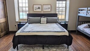 A bedroom with a large bed, two bedside tables, a window with a view, and a bunk bed in the corner.