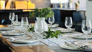 A dining table set with plates, cutlery, and wine glasses, with a vase of greenery in the center.