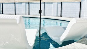 A pool area with white lounge chairs and a large umbrella.
