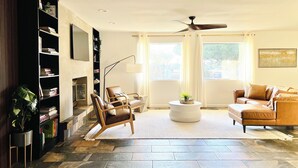 A living room with a fireplace, a bookshelf, two leather sofas, a coffee table, and a ceiling fan.