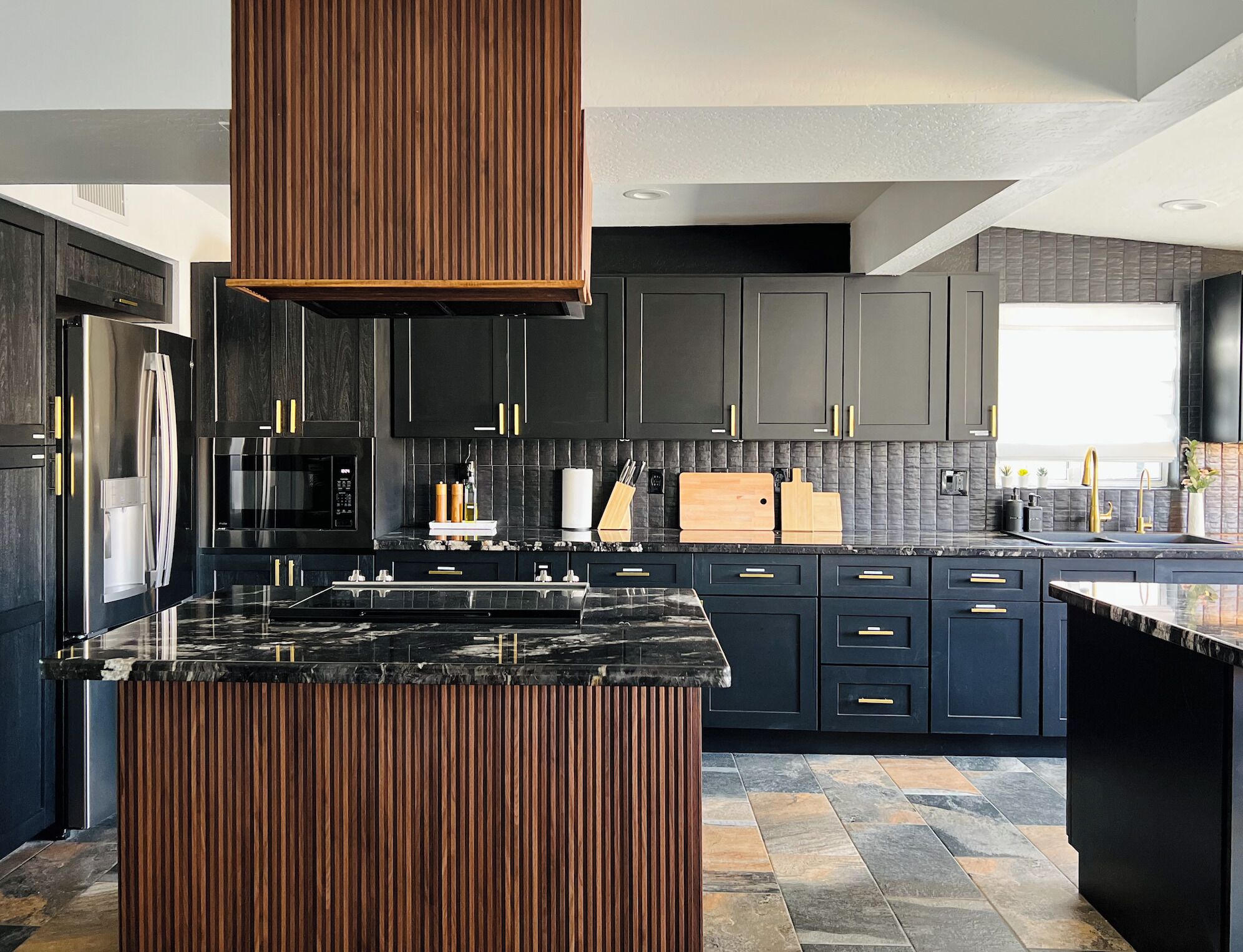 A modern kitchen with dark cabinetry, a central island, and a stone backsplash.