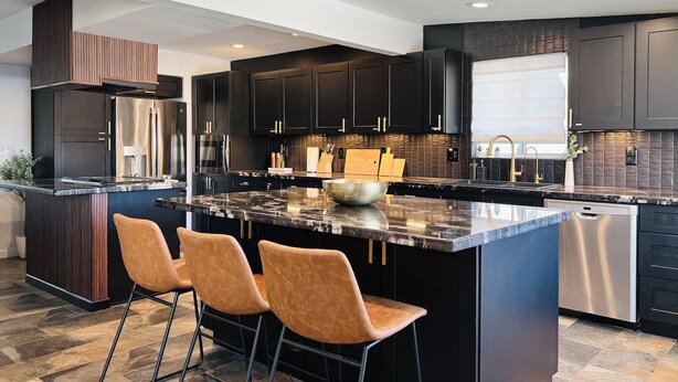 A modern kitchen with dark cabinetry, a central island with bar stools, stainless steel appliances, and a tiled backsplash.