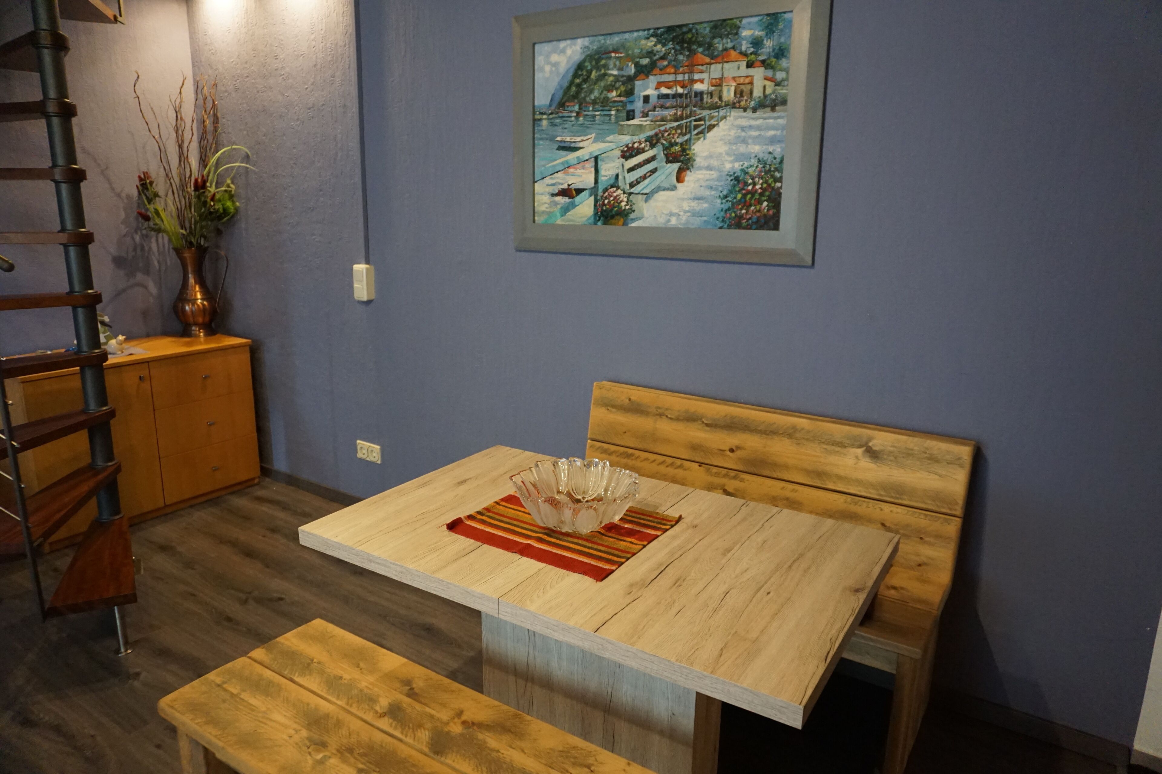 Un comedor con una mesa de madera, un banco y un cuadro en la pared.