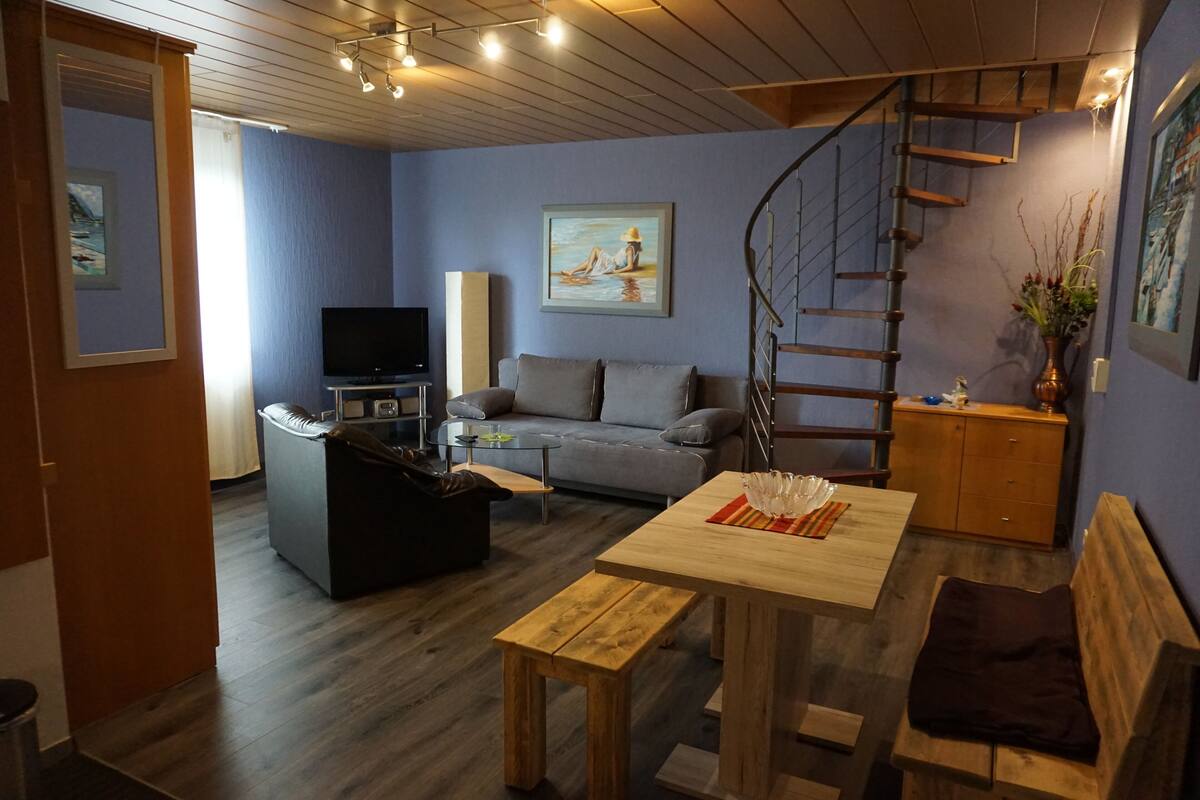 A living room with a sofa, a wooden table, a TV, and a staircase.