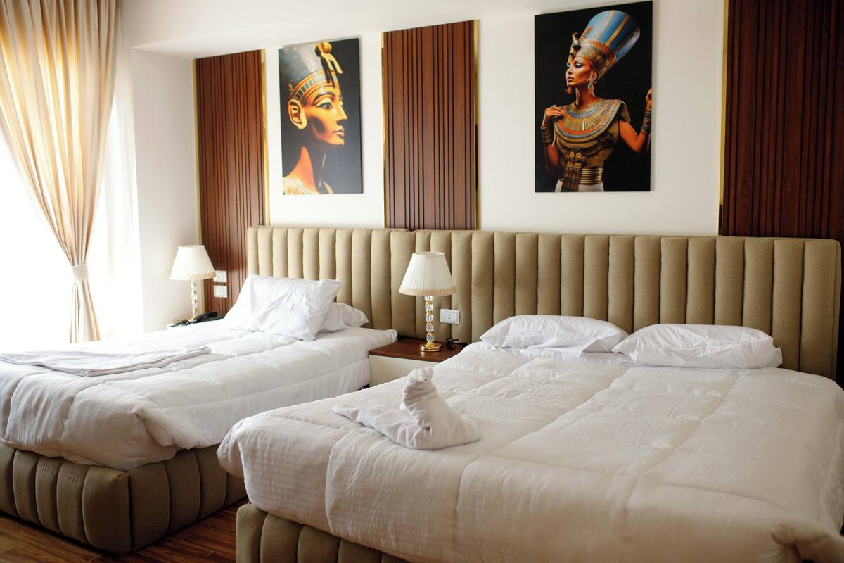 A hotel room with two beds, a wooden headboard, and Egyptian-themed artwork on the walls.