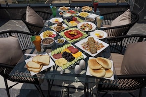A table set with various food items including bread, cheese, and vegetables, surrounded by wicker chairs.